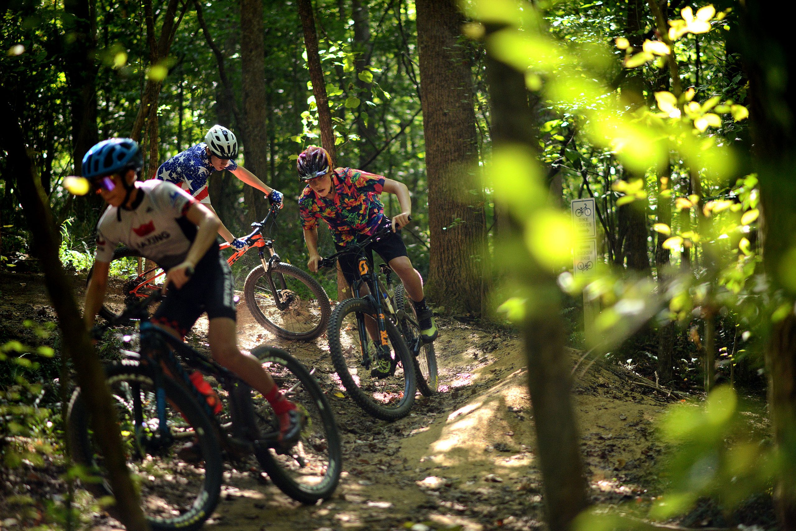 Three young riders flowing down a sunlit Piedmont trail